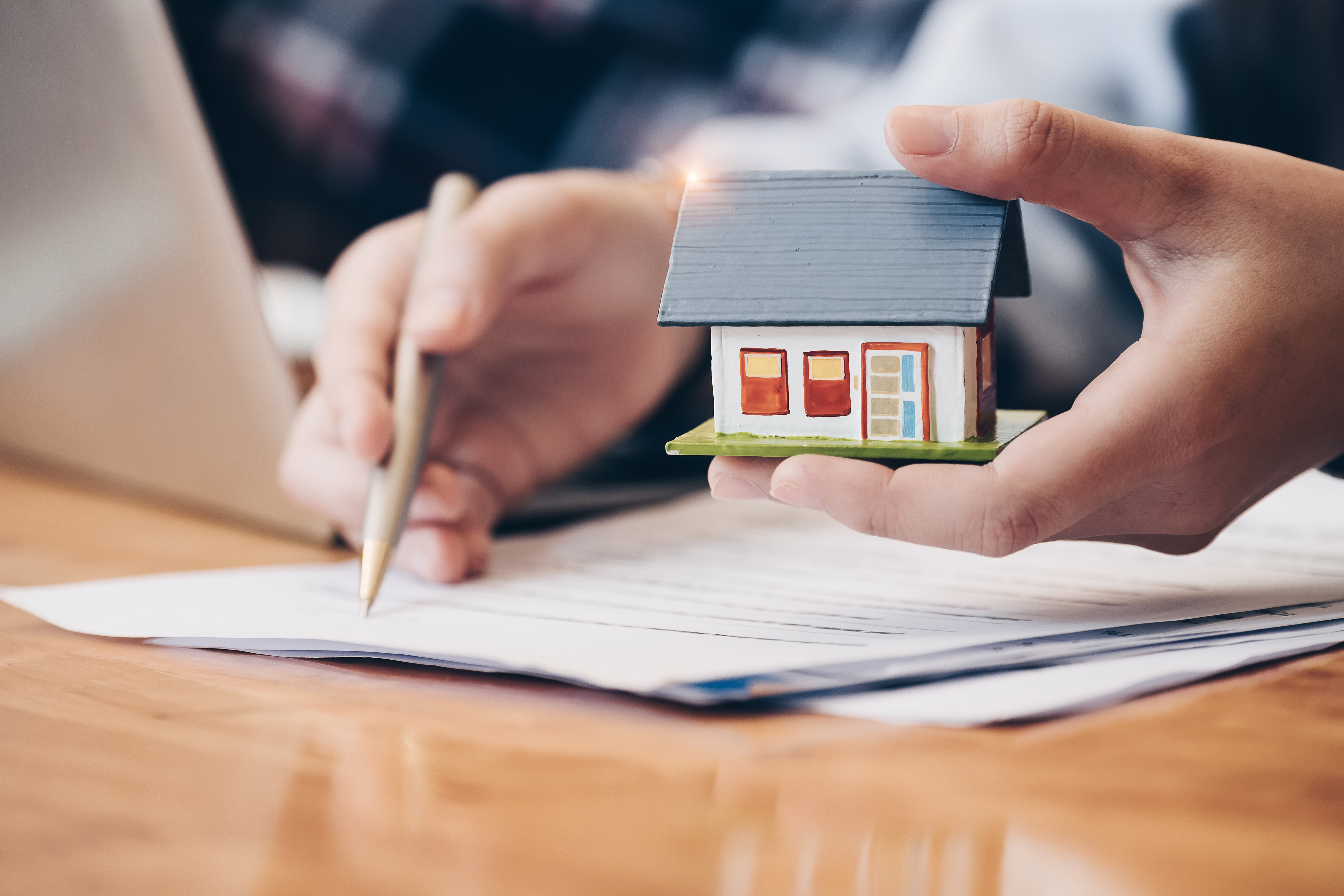 Person holding small house and writing on paper with pen